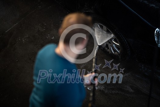 Young man washing his beloved car carefully in a manual car wash to prevent any damage and detail it properly Young man washing his beloved car carefully in a manual car wash to prevent any damage and detail it properly