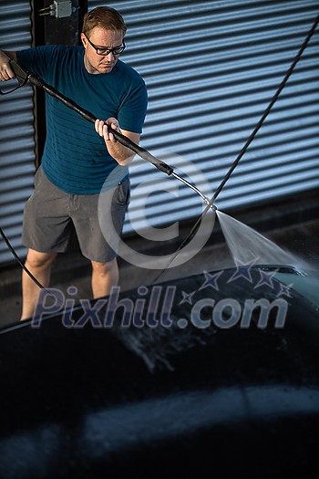 Young man washing his beloved car carefully in a manual car wash to prevent any damage and detail it properly Young man washing his beloved car carefully in a manual car wash to prevent any damage and detail it properly
