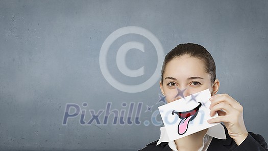 Pretty young girl holding white card with drawn smile showing tongue Pretty young girl holding white card with drawn smile showing tongue
