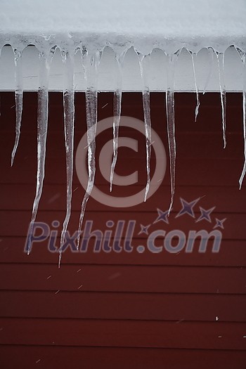 Icicles on the roof of a red house in Norway. melting icicles. natural ice formation in winter time. Icicles on the roof of a red house in Norway. melting icicles. natural ice formation in winter time.