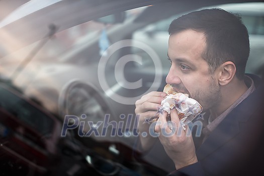 Handsome young man eating a hurried lunch in his car (color toned image; shallow DOF) Handsome young man eating a hurried lunch in his car (color toned image; shallow DOF)