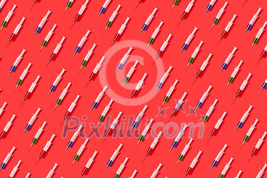 Horizontal health-care pattern from disposable plastic needles with red, green and blue liquid or vaccine on a red background with soft shadow. Flat lay. Horizontal health-care pattern from disposable plastic needles with red, green and blue liquid or vaccine on a red background with soft shadow. Flat lay.