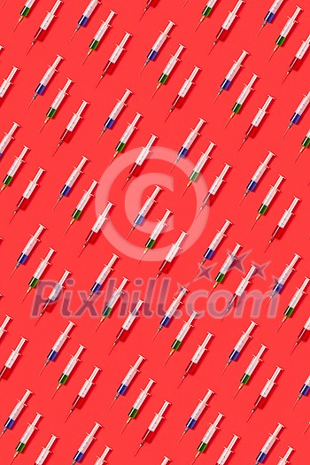 Vertical medicinal pattern from surgical disposable syringes with red, green and blue serum or drugs for injections on a red background, soft shadows. Vertical medicinal pattern from surgical disposable syringes with red, green and blue serum or drugs for injections on a red background, soft shadows.