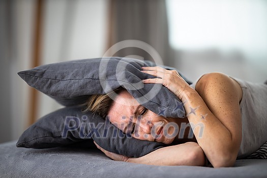 Sleepless lady covering ears with pillow. Noisy neighbors, tinnitus, insomnia or stress concept. Tired woman can't sleep. Awake in bed after coming home from her shift, work. Sleepless lady covering ears with pillow. Noisy neighbors, tinnitus, insomnia or stress concept. Tired woman can't sleep. Awake in bed after coming home from her shift, work.