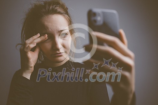 Young woman holding a phone, tired and exhausted, blue light straining her eyes, messing up her circadian rhytm Young woman holding a phone, tired and exhausted, blue light straining her eyes, messing up her circadian rhytm