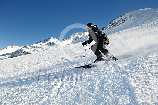 skier skiing downhill on fresh powder snow with sun and mountains in background skier skiing downhill on fresh powder snow with sun and mountains in background