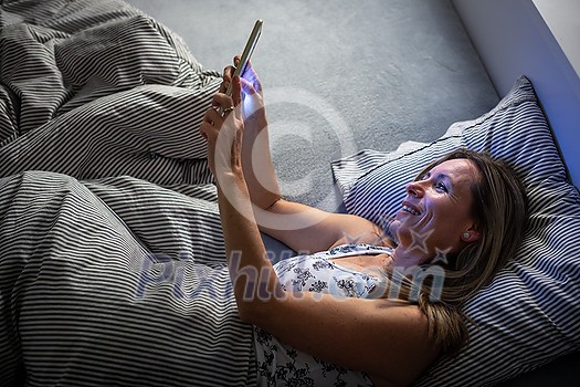 Pretty, middle-aged woman using her tablet computer before sleep in bed in the evening Pretty, middle-aged woman using her tablet computer before sleep in bed in the evening