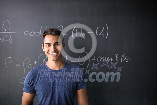 Students in a classroom - handsome student solving a math problem on a blackboard during math class Students in a classroom - handsome student solving a math problem on a blackboard during math class