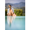 Young Beautiful Suntanned Woman wearing sunglasses relaxing next to a Swimming Pool  on a lovely Summer Day
