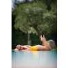 Young Beautiful Suntanned Woman wearing sunglasses relaxing next to a Swimming Pool  on a lovely Summer Day