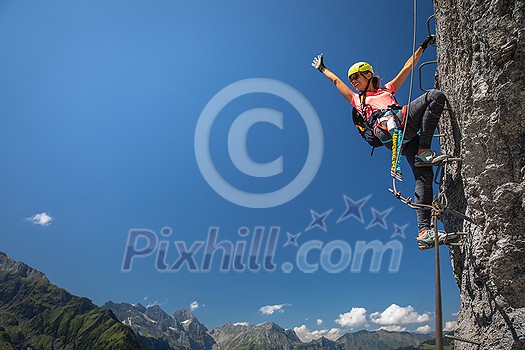 Pretty, female climber on a via ferrata - climbing on a rock in Swiss Alps