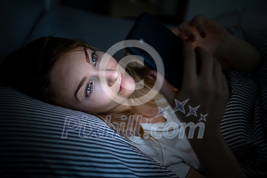 Young woman in bed holding a phone, tired and exhausted, blue light straining her eyes, messing up her circadian rhytm Young woman in bed holding a phone, tired and exhausted, blue light straining her eyes, messing up her circadian rhytm