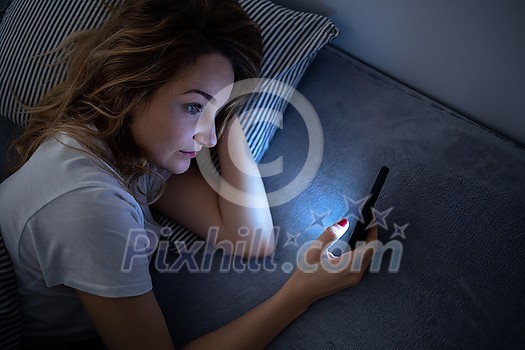Young woman in bed holding a phone, tired and exhausted, blue light straining her eyes, messing up her circadian rhytm Young woman in bed holding a phone, tired and exhausted, blue light straining her eyes, messing up her circadian rhytm