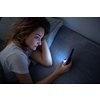 Young woman in bed holding a phone, tired and exhausted, blue light straining her eyes, messing up her circadian rhytm