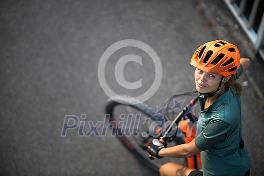 Pretty, young woman with her mountain bike going for a ride past the city limits, getting the daily cardio dose Pretty, young woman with her mountain bike going for a ride past the city limits, getting the daily cardio dose
