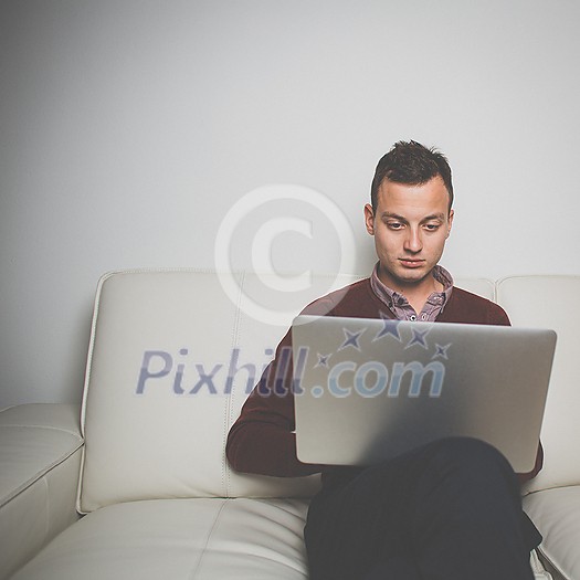 Sleepy young man sitting on a sofa and trying to get some work done on his laptop computer, yawning Sleepy young man sitting on a sofa and trying to get some work done on his laptop computer, yawning