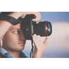 Handsome young photographer using his modern DSLR outdoors, against lovely sky backdrop (color toned image;shallow DOF)