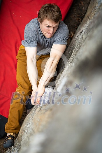 A rock climber climbing on a boulder rock outdoors. Group of friends involved in sports outside. A rock climber climbing on a boulder rock outdoors. Group of friends involved in sports outside.