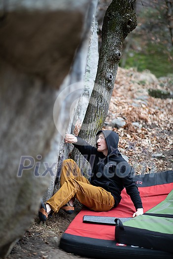 A rock climber climbing on a boulder rock outdoors. Group of friends involved in sports outside.