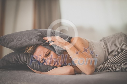 Sleepless lady covering ears with pillow. Noisy neighbors, tinnitus, insomnia or stress concept. Tired woman can't sleep. Awake in bed after coming home from her shift, work. Sleepless lady covering ears with pillow. Noisy neighbors, tinnitus, insomnia or stress concept. Tired woman can't sleep. Awake in bed after coming home from her shift, work.