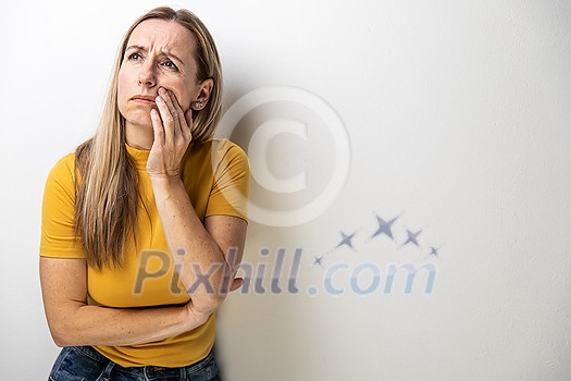 Mid-aged woman touching her cheek/mouth with painful expression because of toothache/dental issue Mid-aged woman touching her cheek/mouth with painful expression because of toothache/dental issue