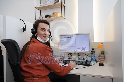 Female call center operator talking to a customer. Businesswoman in mask at the workplace in the modern office. Social distance and safety outbreak new normal concept Female call center operator talking to a customer. Businesswoman in mask at the workplace in the modern office. Social distance and safety outbreak new normal concept