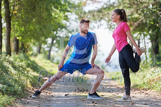 young happy couple enjoying in a healthy lifestyle warming up and stretching before jogging on a country road through the beautiful sunny forest, exercise and fitness concept young happy couple enjoying in a healthy lifestyle warming up and stretching before jogging on a country road through the beautiful sunny forest, exercise and fitness concept
