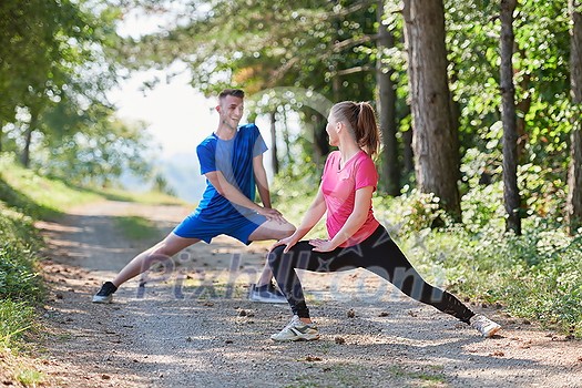 young happy couple enjoying in a healthy lifestyle warming up and stretching before jogging on a country road through the beautiful sunny forest, exercise and fitness concept young happy couple enjoying in a healthy lifestyle warming up and stretching before jogging on a country road through the beautiful sunny forest, exercise and fitness concept