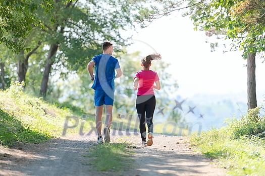 young happy couple enjoying in a healthy lifestyle while jogging on a country road through the beautiful sunny forest, exercise and fitness concept young happy couple enjoying in a healthy lifestyle while jogging on a country road through the beautiful sunny forest, exercise and fitness concept