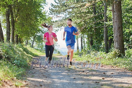 young happy couple enjoying in a healthy lifestyle while jogging on a country road through the beautiful sunny forest, exercise and fitness concept young happy couple enjoying in a healthy lifestyle while jogging on a country road through the beautiful sunny forest, exercise and fitness concept