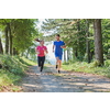 young happy couple enjoying in a healthy lifestyle while jogging on a country road through the beautiful sunny forest, exercise and fitness concept