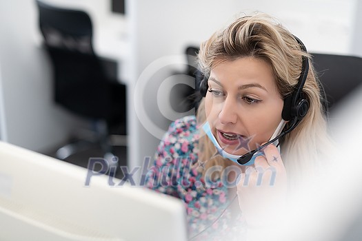 Female call center operator talking to a customer. Businesswoman in mask at the workplace in the modern office. Social distance and safety outbreak new normal concept Female call center operator talking to a customer. Businesswoman in mask at the workplace in the modern office. Social distance and safety outbreak new normal concept