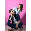 a young couple sitting on the floor while posing in front of a pink background
