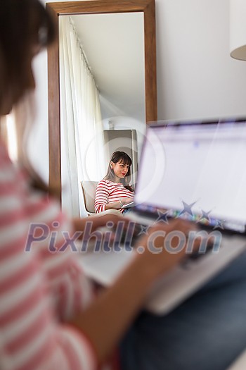 Successful young business woman sitting in a designer chair, working from home. Portrait of happy entrepreneur working on a laptop computer. Doing business remotely from the comfort of her home. Successful young business woman sitting in a designer chair, working from home. Portrait of happy entrepreneur working on a laptop computer. Doing business remotely from the comfort of her home.