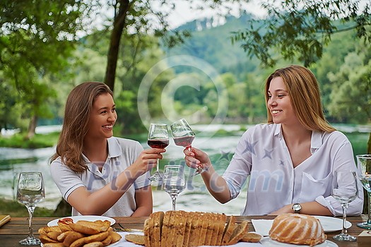 two young happy girlfriends having picnic french dinner party outdoor during summer holiday vacation near the river at beautiful nature