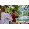group of happy friends toasting red wine glass while having picnic french dinner party outdoor during summer holiday vacation near the river at beautiful nature