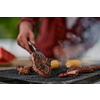 Man cooking tasty food on barbecue grill for outdoor french dinner party near the river on beautiful summer evening in nature