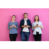 a group of friends have fun and dance while using a cell phone and headphones isolated on a pink background