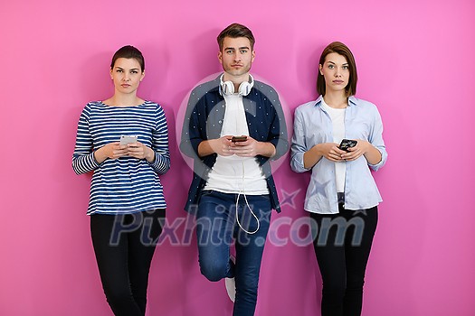 a group of friends have fun and dance while using a cell phone and headphones isolated on a pink background