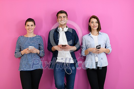 a group of friends have fun and dance while using a cell phone and headphones isolated on a pink background