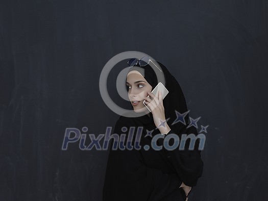 Young muslim businesswoman in traditional clothes or abaya talking on the smartphone. Arab woman in front of black chalkboard and representing techology, islamic fashion and Ramadan kareem concept Young muslim businesswoman in traditional clothes or abaya talking on the smartphone. Arab woman in front of black chalkboard and representing techology, islamic fashion and Ramadan kareem concept