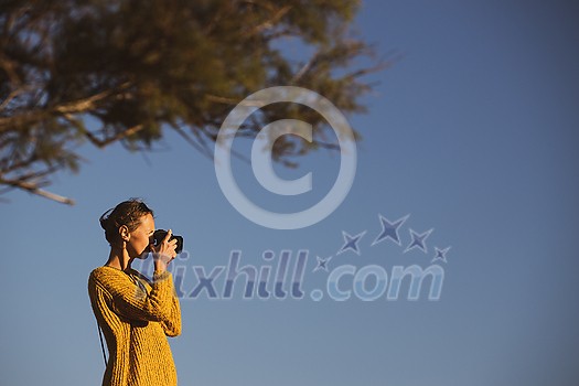 Pretty, young woman with a mirrorless camera, taking photos by the sea Pretty, young woman with a mirrorless camera, taking photos by the sea