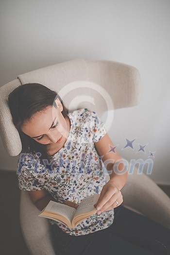 Cute young woman reading a book in a designer chair - color toned image, shallow DOF Cute young woman reading a book in a designer chair - color toned image, shallow DOF