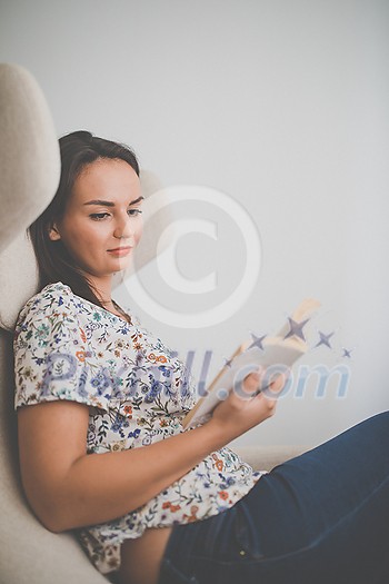 Cute young woman reading a book in a designer chair - color toned image, shallow DOF Cute young woman reading a book in a designer chair - color toned image, shallow DOF