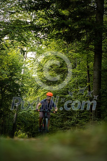 Young man with his mountain bike going for a ride past the city limits in a lovely forest, getting the daily cardio dose - biker out of focus with sharp trees behind him Young man with his mountain bike going for a ride past the city limits in a lovely forest, getting the daily cardio dose - biker out of focus with sharp trees behind him