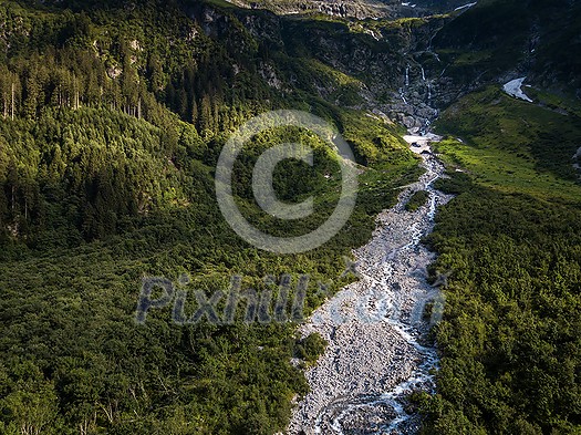 Aerial top view of summer green trees in forest with a splendid mountain river in Swiss Alps