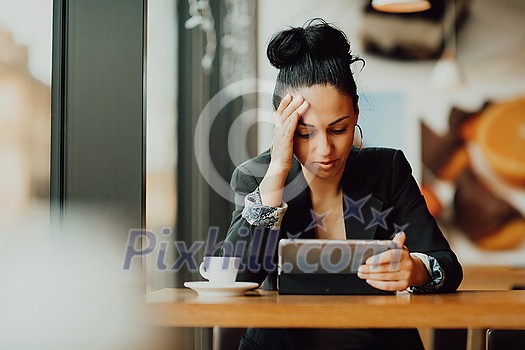 Young Latin woman with sad face sitting in the coffee shop at wooden table, drinking coffee and using a laptop. Young Latin woman with sad face sitting in the coffee shop at wooden table, drinking coffee and using a laptop.