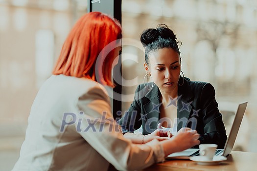 One-on-one meeting.Two young businesswomen sitting at a table in a cafe. Girl shows colleague information on the laptop screen. Girl using smartphone, blogging. Teamwork, business meeting. Freelancers working.