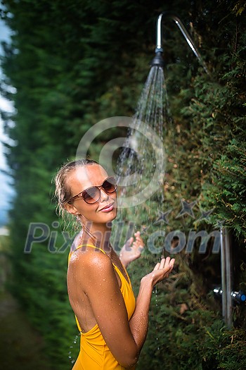 Beautiful young woman taking a shower outdoors. Attractive young woman in yellow one-piece enjoys shower on hot sunny day after a swim. Heat and refreshment concept. Beautiful young woman taking a shower outdoors. Attractive young woman in yellow one-piece enjoys shower on hot sunny day after a swim. Heat and refreshment concept.
