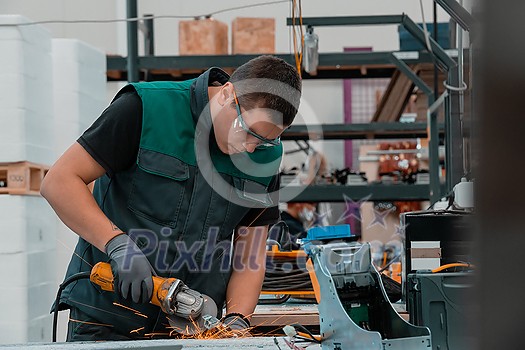 Heavy Industry Engineering Factory Interior with Industrial Worker Using Angle Grinder and Cutting a Metal Tube. Contractor in Safety Uniform and Hard Hat Manufacturing Metal Structures. High quality photo Heavy Industry Engineering Factory Interior with Industrial Worker Using Angle Grinder and Cutting a Metal Tube. Contractor in Safety Uniform and Hard Hat Manufacturing Metal Structures. High quality photo